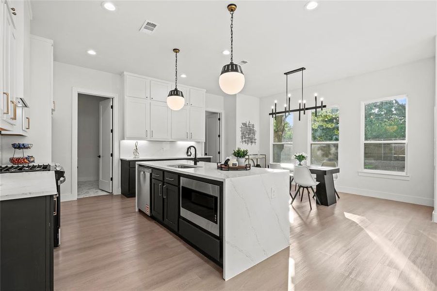 Kitchen featuring appliances with stainless steel finishes, healthy amount of natural light, recessed lighting, light wood-type flooring, and light stone countertops