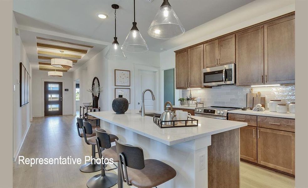 Contemporary kitchen featuring a large island with seating, stainless steel appliances, wood-finish cabinetry, and a tile backsplash