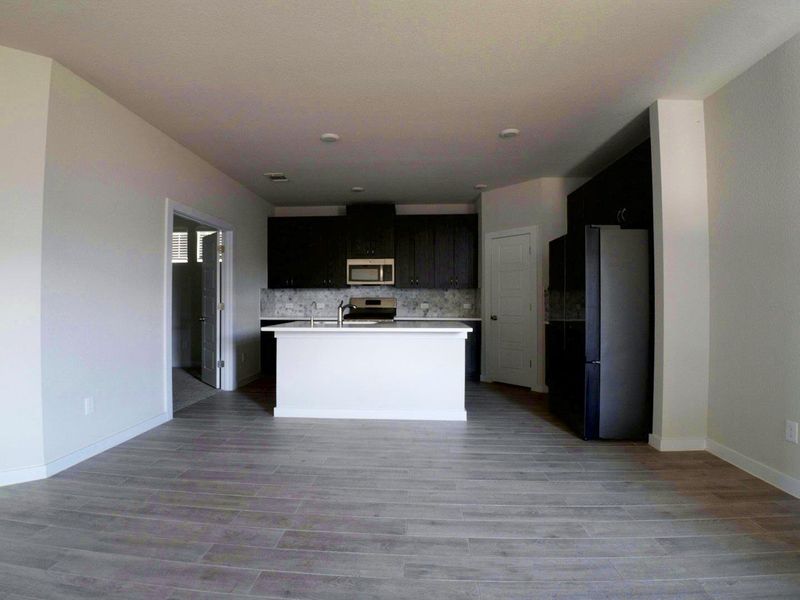 Kitchen featuring light countertops, appliances with stainless steel finishes, open floor plan, tasteful backsplash, and dark cabinets Kitchen featuring light countertops, appliances with stainless steel finishes, open floor plan, tasteful backsplash, and dark cabinets