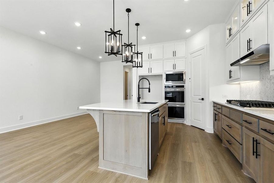Kitchen with recessed lighting, a kitchen island with sink, hanging light fixtures, white cabinetry, and light wood-style floors Kitchen with recessed lighting, a kitchen island with sink, hanging light fixtures, white cabinetry, and light wood-style floors