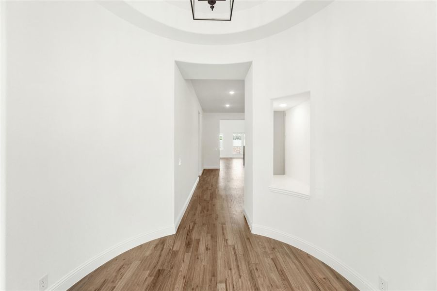 Entryway foyer with round tray ceiling, pendant light, hardwood floors, and hallway leading to main living area