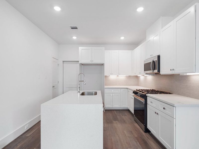 Experience modern elegance in this beautifully designed kitchen, featuring sleek white cabinetry, a spacious island with a chic sink, and top-of-the-line stainless steel appliances, all set against a backdrop of warm, inviting flooring—ideal for creating your dream home.Photo Disclaimer: Photos are representative of the community and may depict a similar floor plan, model home, or previously completed residence.
