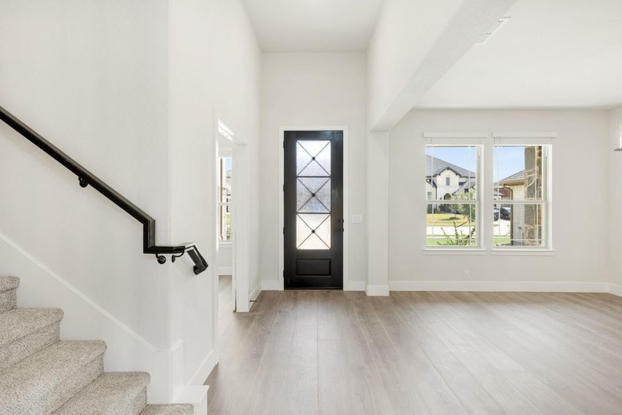 Bright home entryway with black glass-panel front door, light wood floors, and staircase with black railing