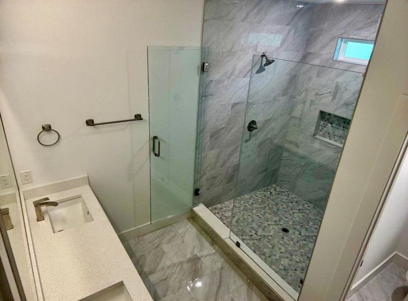 Contemporary bathroom featuring a spacious glass-enclosed shower, a wide vanity with an integrated sink, and large format floor tiling