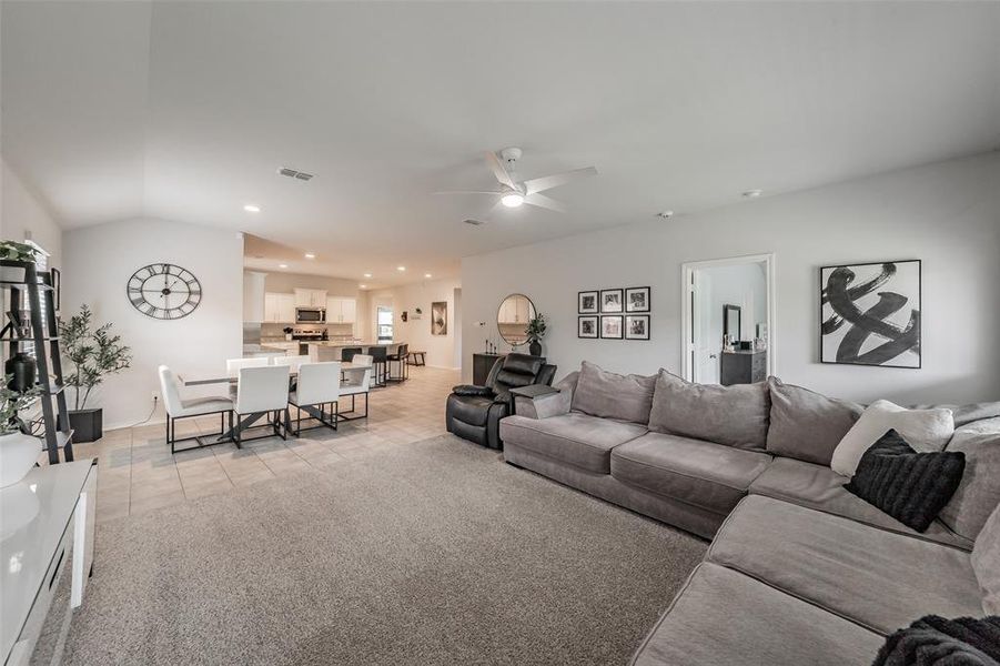 Open-concept living space featuring a carpeted area, tile flooring, and a ceiling fan