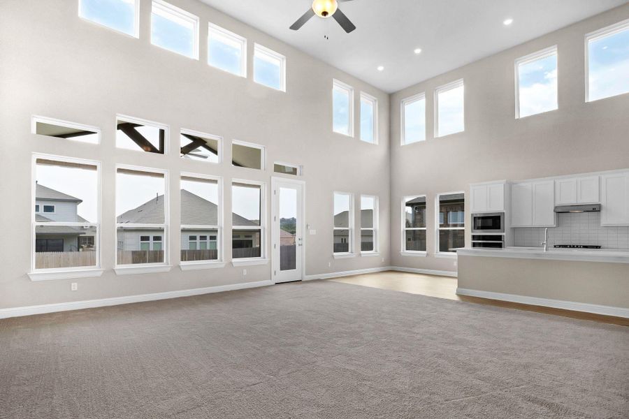Unfurnished living room with visible vents, baseboards, light colored carpet, a high ceiling, and ceiling fan Unfurnished living room with visible vents, baseboards, light colored carpet, a high ceiling, and ceiling fan