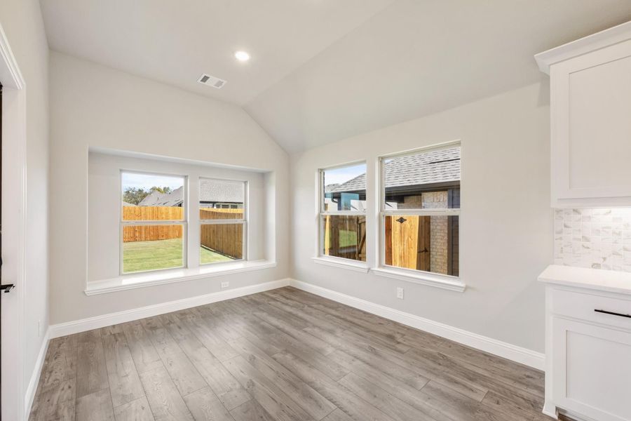 Bright dining area with vaulted ceiling, hardwood floors, and large windows overlooking backyard Bright dining area with vaulted ceiling, hardwood floors, and large windows overlooking backyard