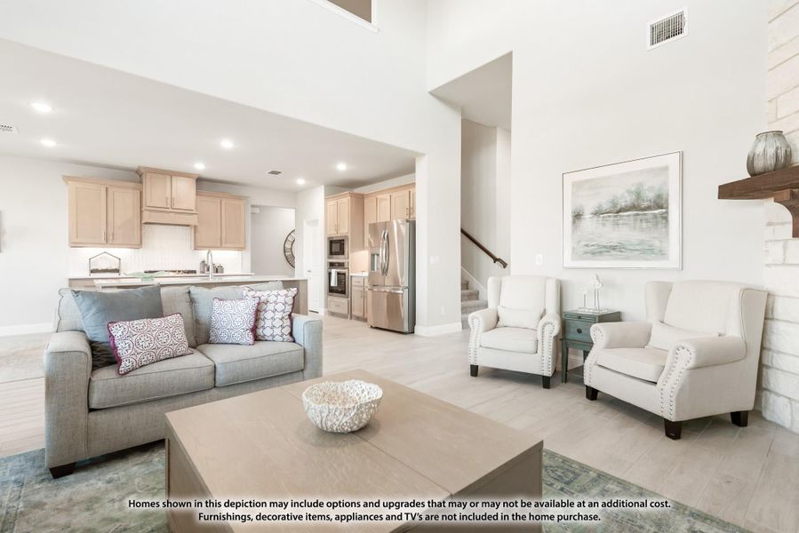 Open-concept living room with high ceilings, sofa, and armchairs, open to kitchen with stainless appliances and light wood cabinets.