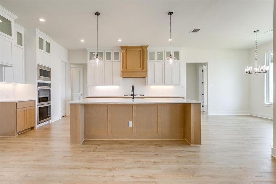 Kitchen with hanging light fixtures, a large island with sink, white cabinetry, and light hardwood / wood-style flooring