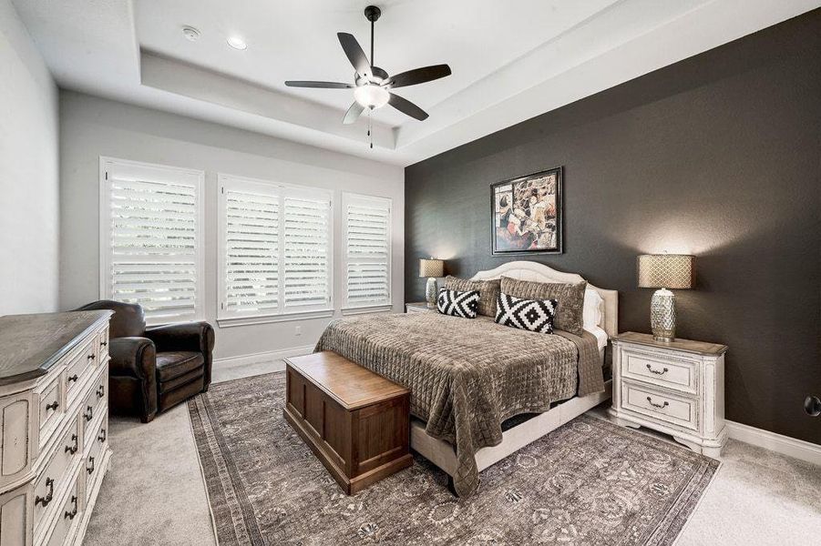 Bedroom with light colored carpet, a ceiling fan, and a raised ceiling Bedroom with light colored carpet, a ceiling fan, and a raised ceiling