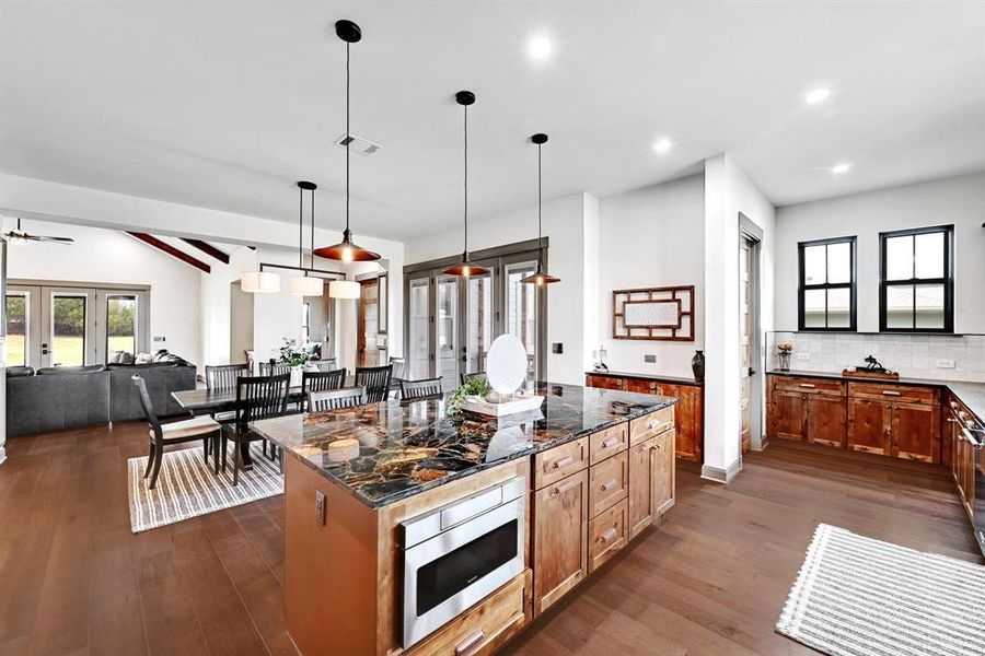 Kitchen with dark wood finished floors, plenty of natural light, dark stone counters, decorative light fixtures, and recessed lighting