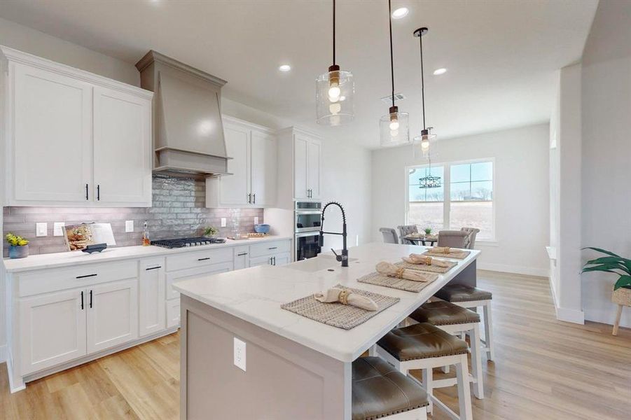 Kitchen with hanging light fixtures, custom range hood, white cabinets, and a center island with sink