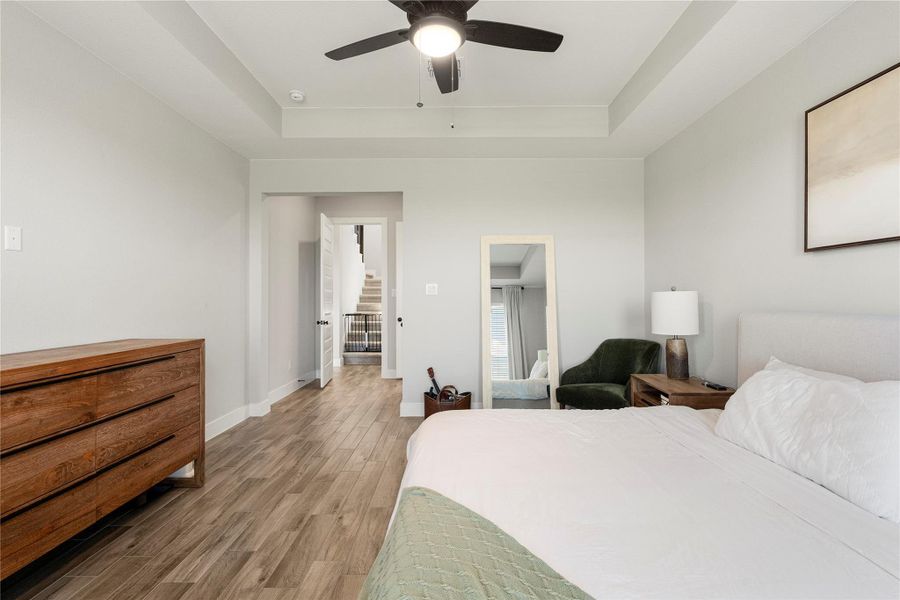 Recessed lighting illuminates this well-lit bedroom featuring a tray ceiling and wood flooring. Recessed lighting illuminates this well-lit bedroom featuring a tray ceiling and wood flooring.