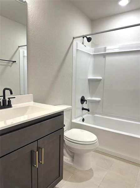 En-suite bath with vanity,  shower combination, tile floors, toilet, and a textured wall