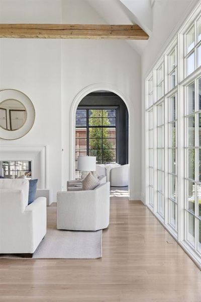 Living area featuring light wood-style floors, high vaulted ceiling, arched walkways, and beam ceiling