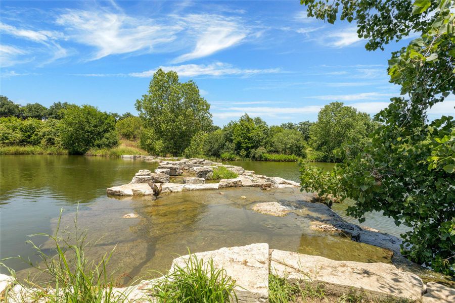 A tranquil river flows past natural stone formations, framed by lush trees under a vibrant sky.