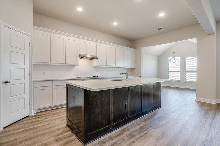 Kitchen featuring a center island with sink, white cabinets, extractor fan, and light hardwood / wood-style flooring