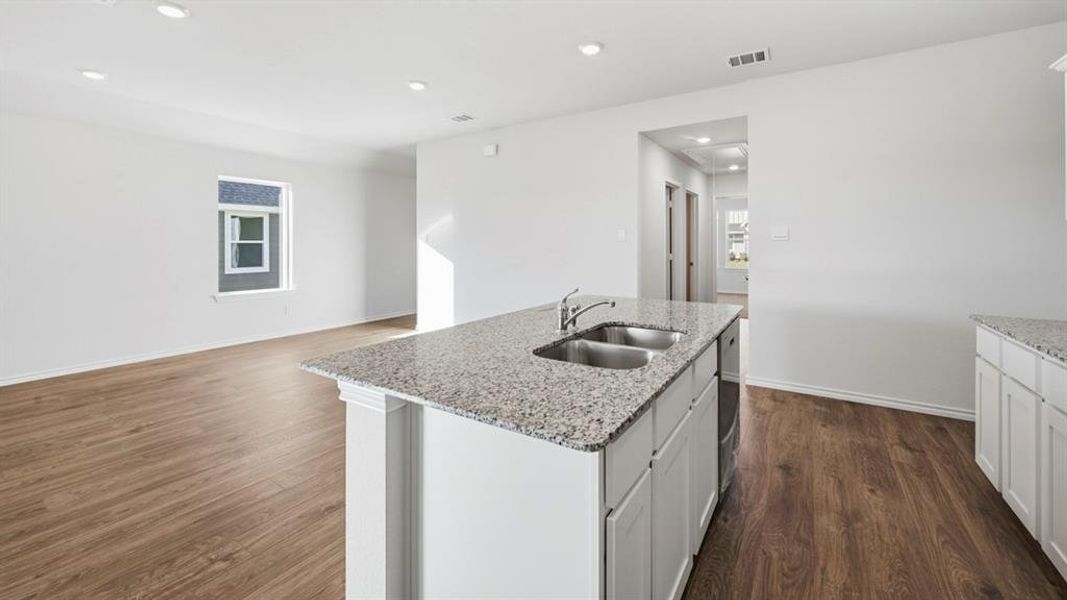 Kitchen with a center island with sink, light stone countertops, white cabinets, recessed lighting, and dark wood-type flooring Kitchen with a center island with sink, light stone countertops, white cabinets, recessed lighting, and dark wood-type flooring