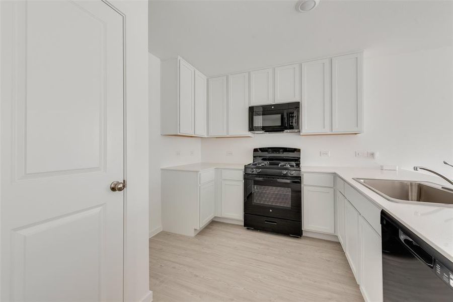 Kitchen with sink, white cabinetry, black appliances, and light wood-type flooring