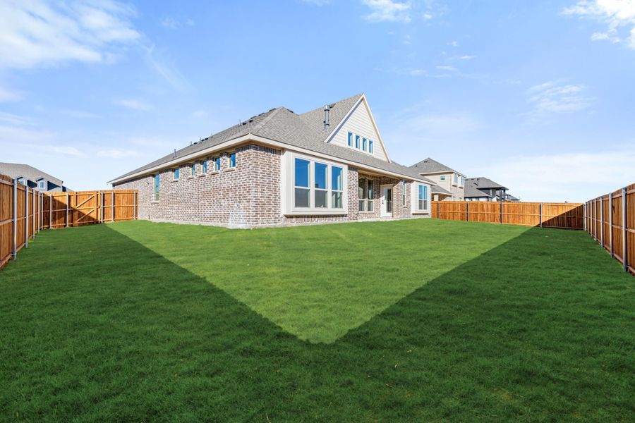 Backyard of two-story brick home with large green lawn and wood privacy fence