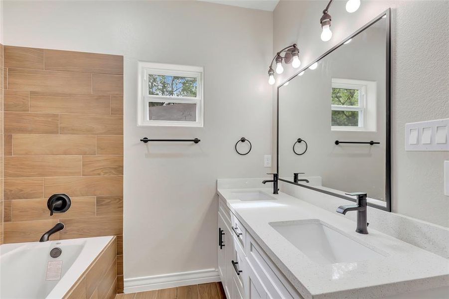 Primary bath vanity with double sink, sleek black faucets and light fixtures.