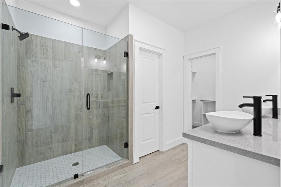 Modern bathroom featuring a large walk-in shower with glass doors, sleek vessel sink on a white countertop, and contemporary fixtures, accented by light wood-look tiles and white walls, offering a clean and minimalist aesthetic.