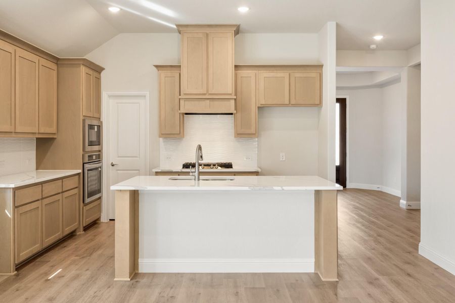 Kitchen with light wood cabinets, white quartz island, stainless steel appliances, and light hardwood floors Kitchen with light wood cabinets, white quartz island, stainless steel appliances, and light hardwood floors