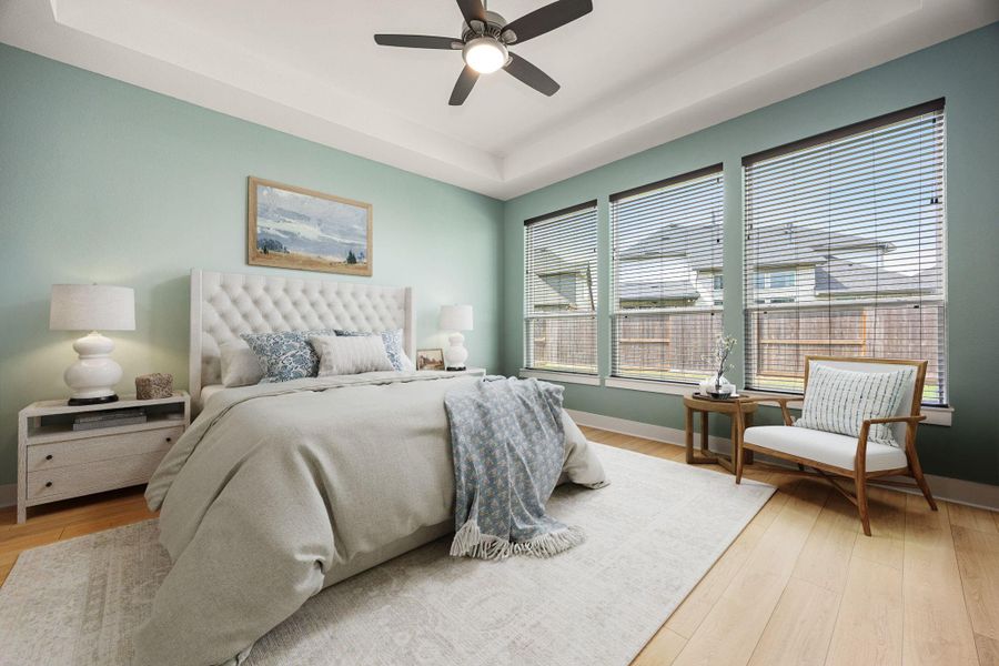 This inviting primary suite showcases a tray ceiling with modern fan, wide-plank wood flooring, and expansive windows that fill the room with natural light. Overlooking the backyard, it offers a bright and relaxing retreat with plenty of space to unwind.