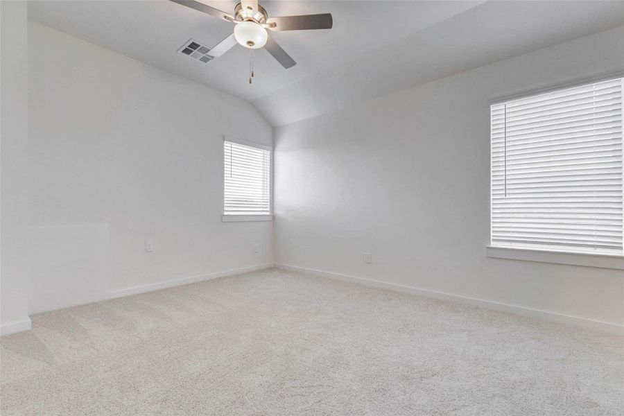 Bright secondary bedroom featuring soft carpet, neutral paint, ceiling fan, and two windows with blinds for natural light. The vaulted ceiling adds a sense of openness, while the simple, fresh finishes make the room easy to furnish as a bedroom, study, or flex space.