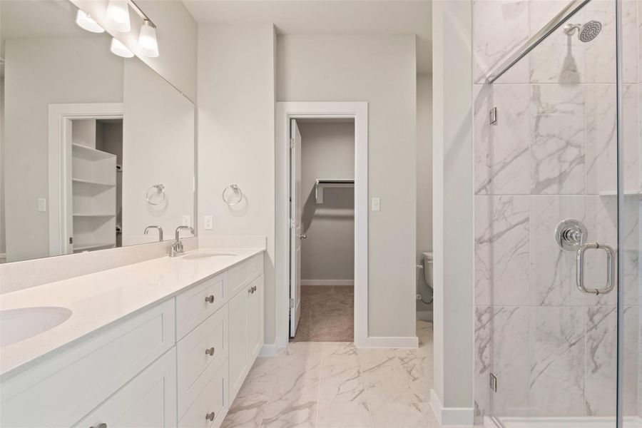 Full bathroom with light marble finish floors, a marble finish shower, a spacious closet, and double vanity