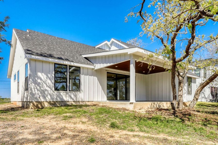 Rear view of property featuring a shingled roof, board and batten siding, a lawn, and covered porch