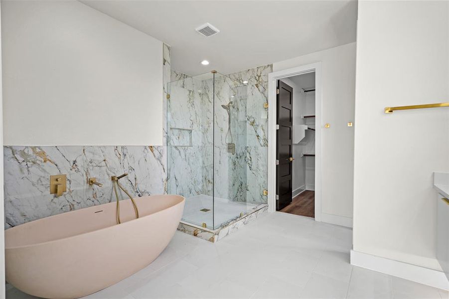 This bathroom features a freestanding bathtub with gold-toned fixtures, a glass-enclosed shower with marble-patterned tile, and light-colored flooring This bathroom features a freestanding bathtub with gold-toned fixtures, a glass-enclosed shower with marble-patterned tile, and light-colored flooring