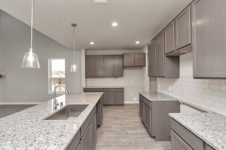 Discover another perspective of this stunning kitchen, sleek back splash, single basin sink, and generously appointed with an abundance of counter space. Sample photo of completed home with similar floor plan. As-built interior colors and selections may vary.