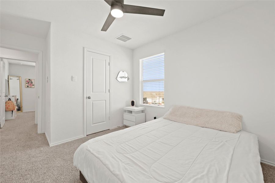 Comfortable upstairs bedroom boasts clean lines, a cooling ceiling fan, and a large window overlooking the neighborhood.