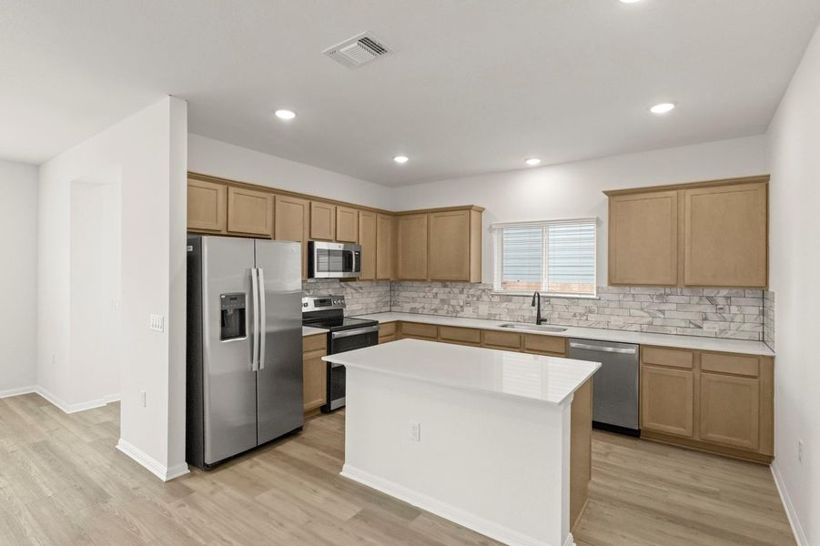 Kitchen with stainless steel appliances, a kitchen island, light wood finished floors, recessed lighting, and tasteful backsplash
