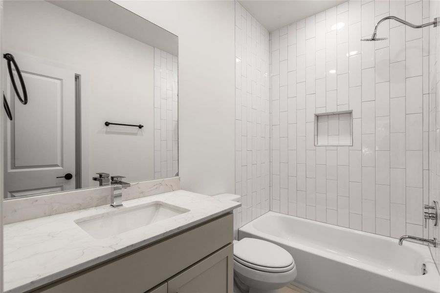 Guest bath setup — vertical stack subway tile surround, built-in shampoo niche, quartz-topped vanity, and clean black hardware accents.
