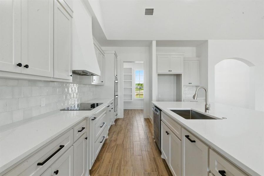 Kitchen with tasteful backsplash, light stone countertops, white cabinetry, wood finished floors, and stainless steel dishwasher Kitchen with tasteful backsplash, light stone countertops, white cabinetry, wood finished floors, and stainless steel dishwasher
