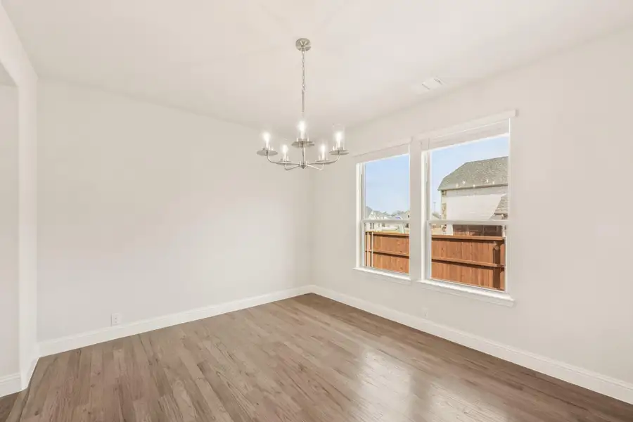 Empty dining room with hardwood floors, chandelier, and double window with backyard view