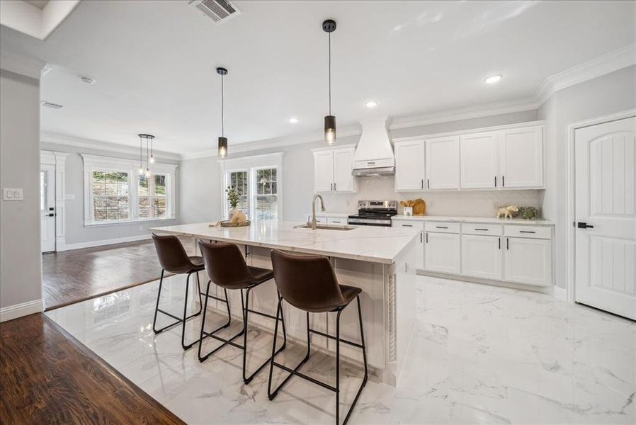 Kitchen featuring white cabinetry, sink, hanging light fixtures, a center island with sink, and custom range hood