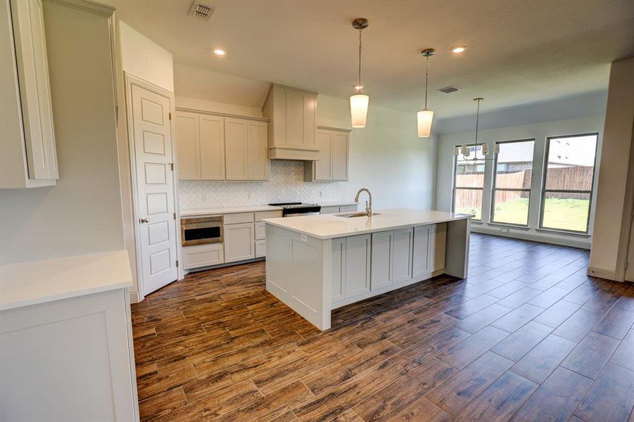 Kitchen with tasteful backsplash, light stone counters, an island with sink, pendant lighting, and dark wood-style floors Kitchen with tasteful backsplash, light stone counters, an island with sink, pendant lighting, and dark wood-style floors