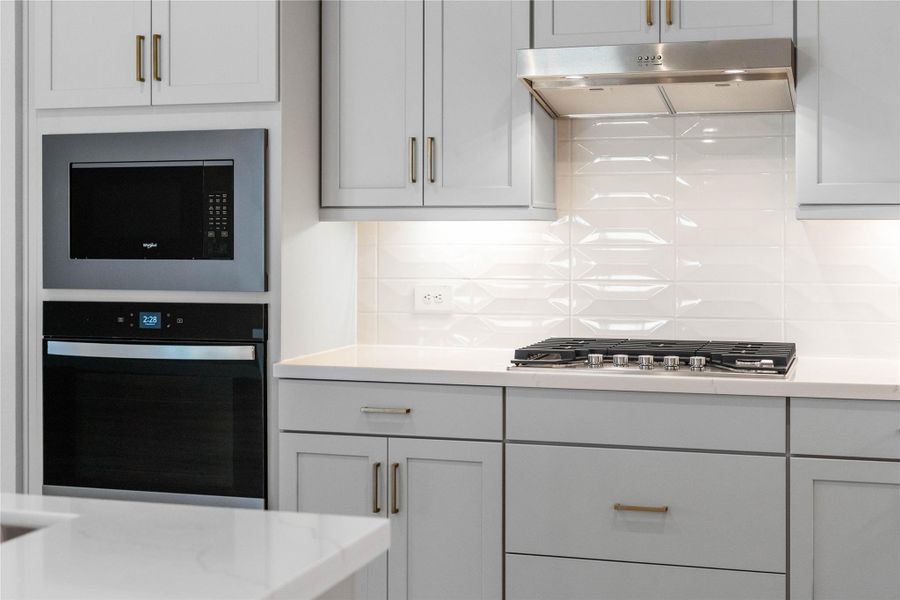 A sleek, built-in oven and microwave stack is seamlessly integrated into the cabinetry, complemented by a matching ventilation hood over the gas cooktop.