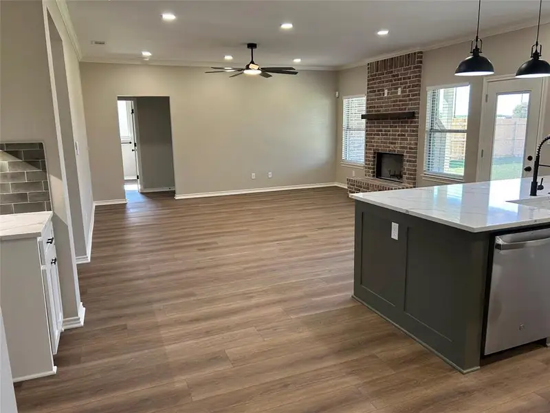 Kitchen with ornamental molding, light stone countertops, stainless steel dishwasher, recessed lighting, and a brick fireplace