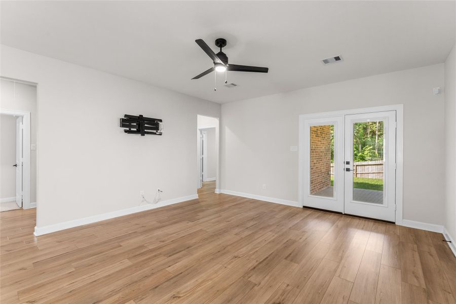 Spacious living room featuring abundant natural light, wood-look flooring, and French doors leading to the covered patio. Enjoy peaceful backyard views with no rear neighbors Spacious living room featuring abundant natural light, wood-look flooring, and French doors leading to the covered patio. Enjoy peaceful backyard views with no rear neighbors