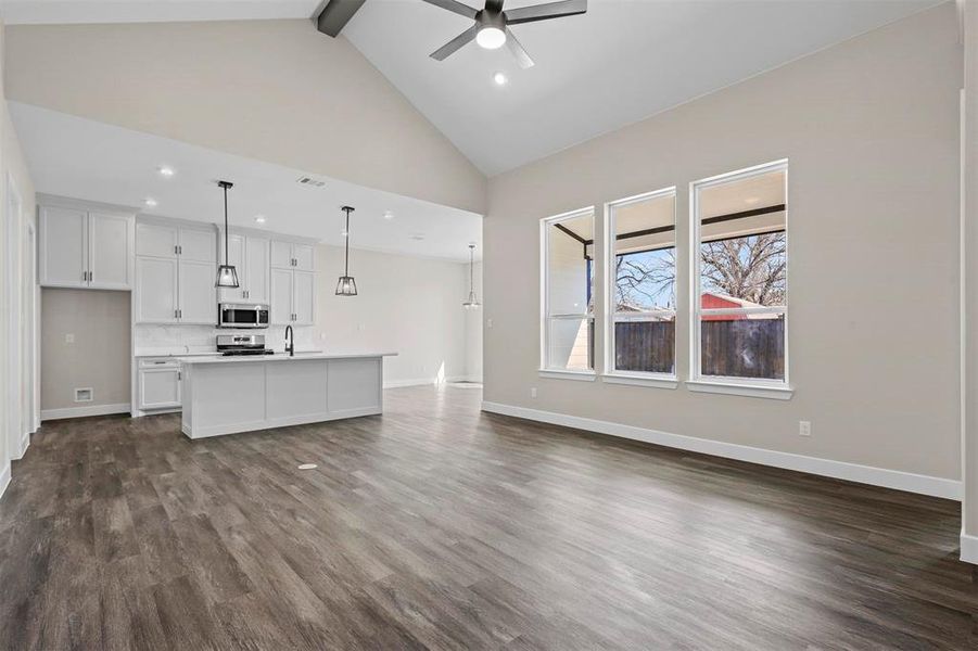 Unfurnished living room with dark hardwood / wood-style flooring, beam ceiling, sink, ceiling fan, and high vaulted ceiling