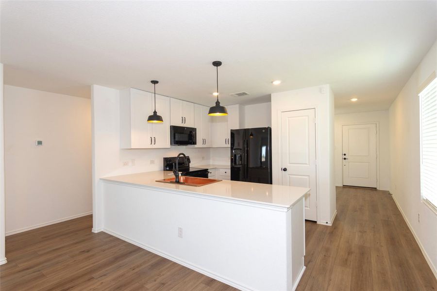Contemporary kitchen featuring white cabinetry, black appliances, quartz countertops, and two pendant lights over the island