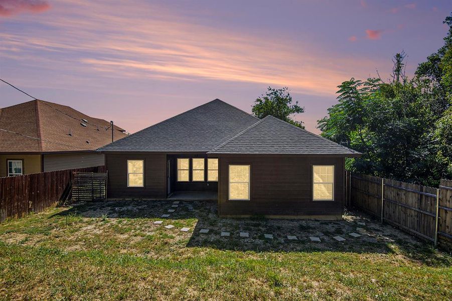 Back of property at dusk with a fenced backyard and roof with shingles