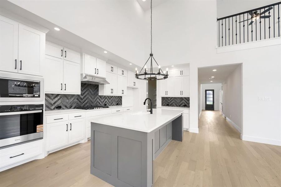 Contemporary kitchen featuring white cabinetry with black hardware, a herringbone pattern tile backsplash, and a central island with a light-toned countertop