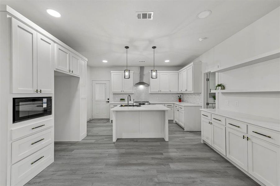 Kitchen with wall chimney exhaust hood, sink, pendant lighting, white cabinetry, and black microwave