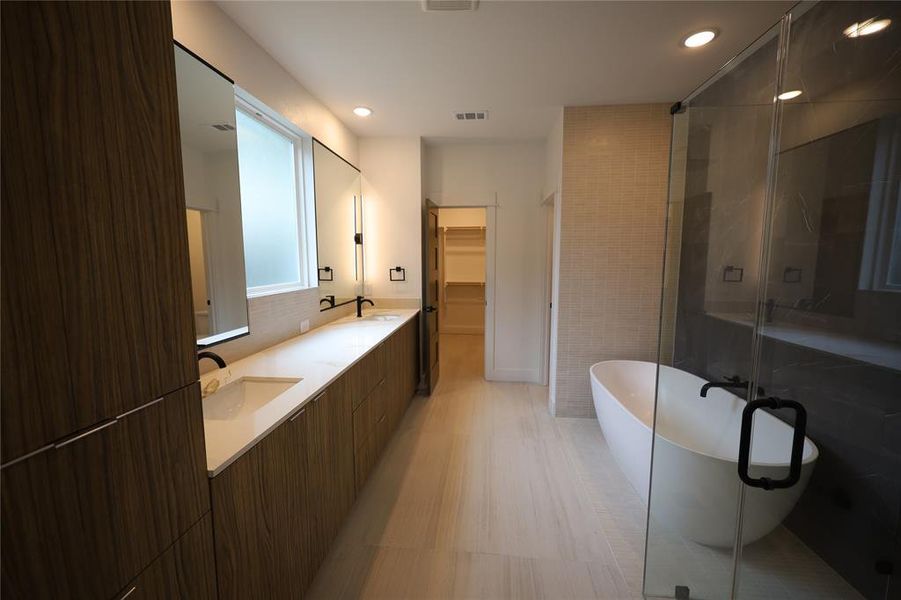 Full bath with a walk in closet, a freestanding tub, a shower stall, double vanity, and tile walls