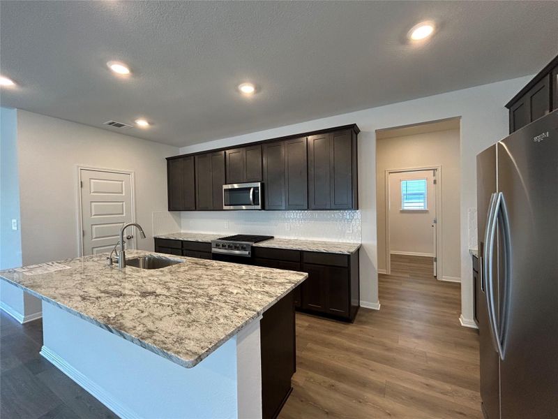 Kitchen featuring stainless steel appliances, light stone countertops, dark wood-style floors, an island with sink, and recessed lighting